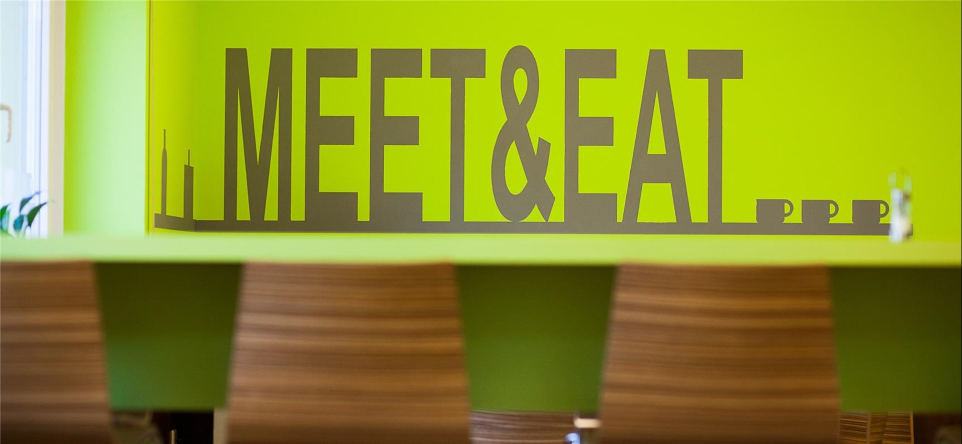 Wand mit englischen Schriftzug Meet and eat, davor eine Theke mit Stühlen 
