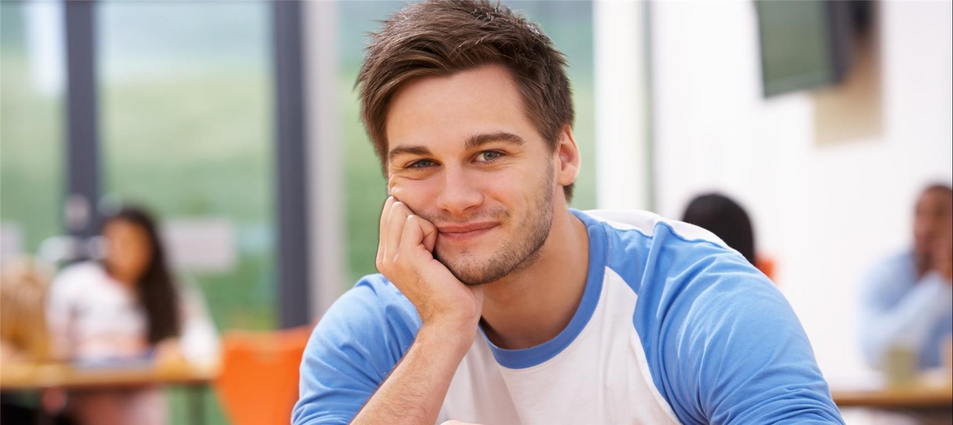 Junger Mann sitzt am Tisch und stützt den Kopf auf